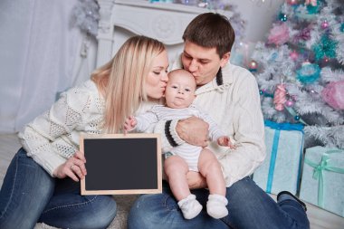 mutlu bir aile rahat bir oturma odasında halı üzerinde oturan boş bir Noel kartı tutan