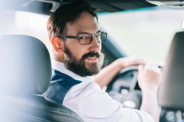 bir arabanın direksiyonuna oturan gülümseyen iş adamı