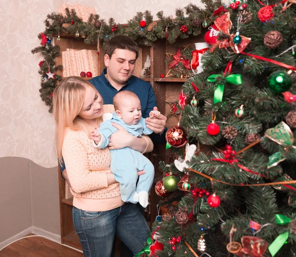 Gelukkige ouders en hun baby staan naast de kerstboom — Stockfoto