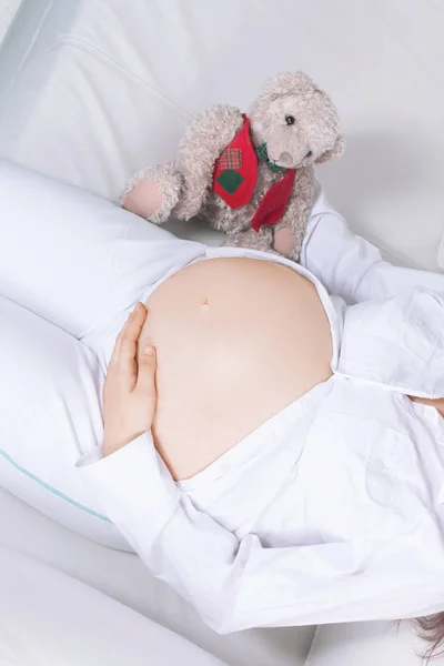 Nahaufnahme. Schöne schwangere Frau mit einem Stofftier auf der Couch liegend. — Stockfoto