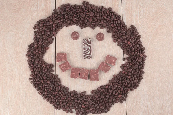 Смешное лицо из зерна черного кофе и шоколада на деревянном b — стоковое фото