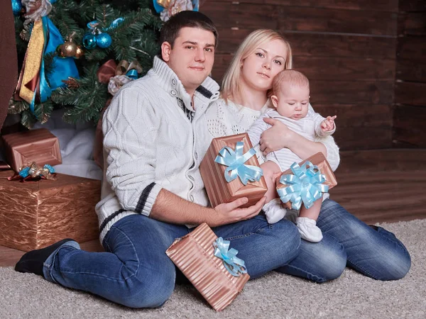 Familia feliz con cajas de regalo sentadas cerca del árbol de Navidad en Nochebuena — Foto de Stock