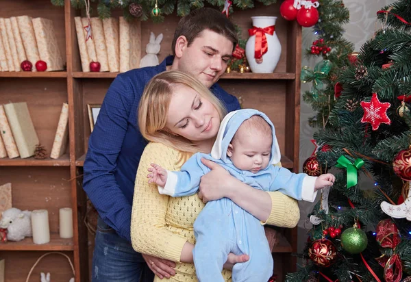 Gelukkige ouders en hun baby staan naast de kerstboom — Stockfoto