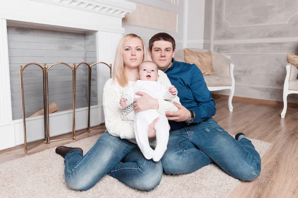 Happy parents and their baby sitting near the fireplace in the cozy living room. — Stock Photo, Image