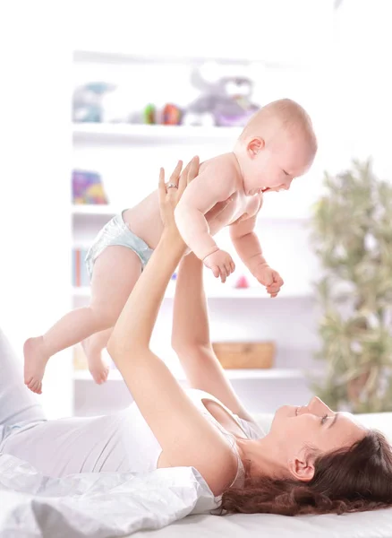 Junge Mutter spielt mit dem Baby auf dem Bett liegend — Stockfoto