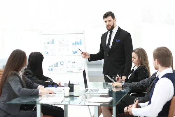 Внимательные деловые партнеры смотрят на успешного предпринимателя указывая на доску в офисе — стоковое фото