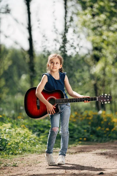 Holčička s kytarou na pozadí v parku — Stock fotografie