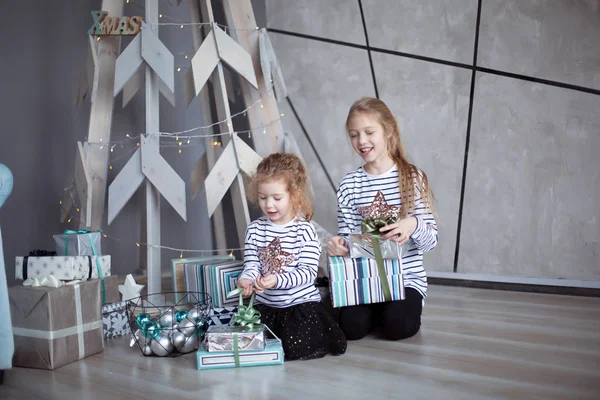 Hermanas pequeñas están mirando regalos de Navidad sentadas en la moderna sala de estar — Foto de Stock