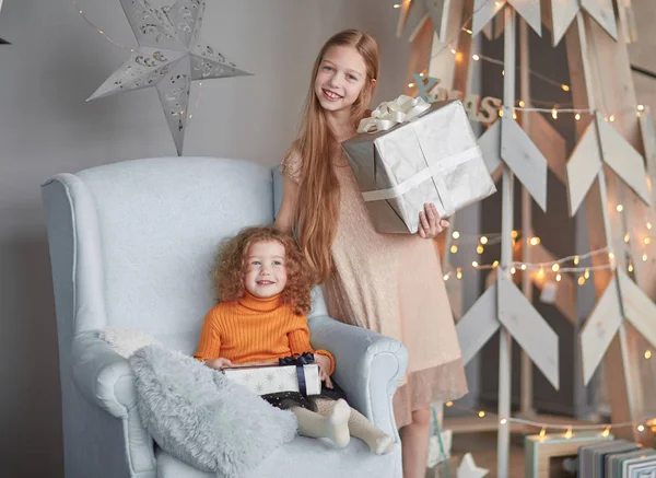 Duas meninas com presentes em pé perto de uma árvore de Natal estilizada — Fotografia de Stock