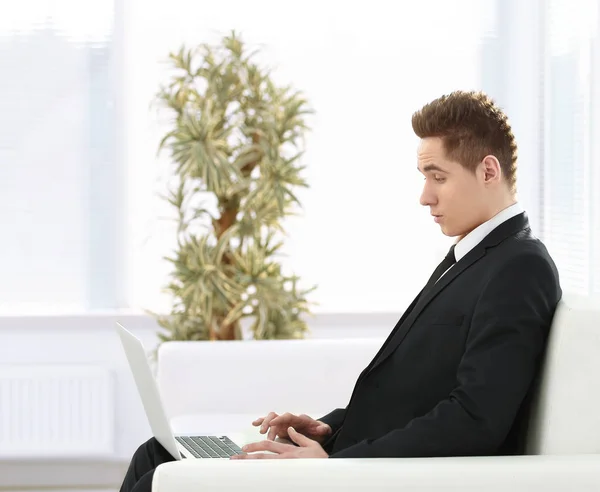 Guapo hombre de negocios escribiendo en el portátil sentado en el vestíbulo de th — Foto de Stock