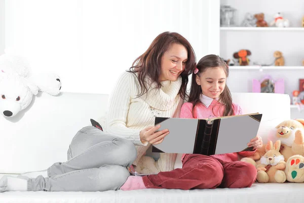 Charmiga mor och dotter en bok som sitter på couch.photo med kopia utrymme — Stockfoto