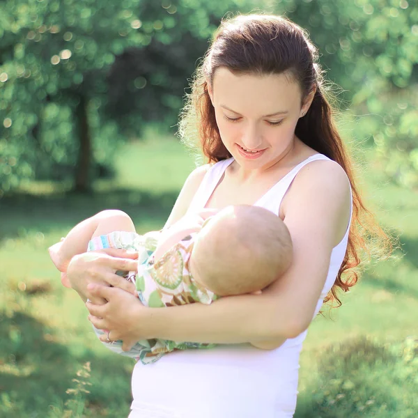 Mujer joven con un bebé en un fondo del parque de la ciudad —  Fotos de Stock