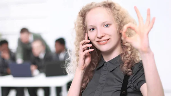 Call center operator beautiful young woman talking on cell phone with the team in the background — Stock Photo, Image