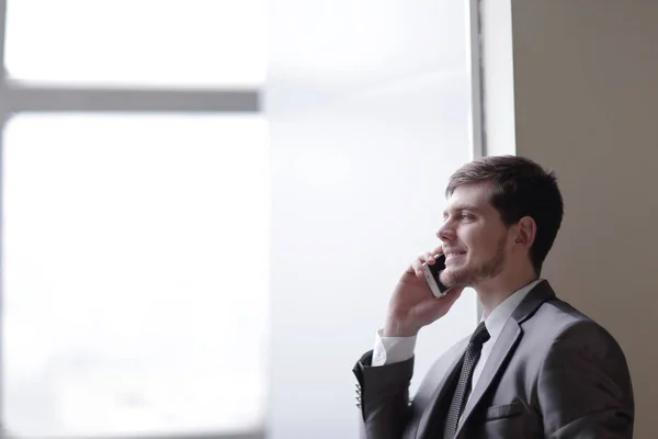 Close up. businessman talking on smartphone while standing near an office window — стоковое фото