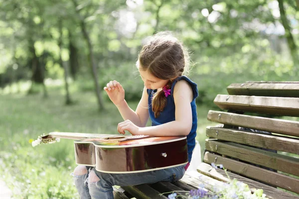 Menina com uma guitarra sentada em um banco em uma cidade Park . — Fotografia de Stock