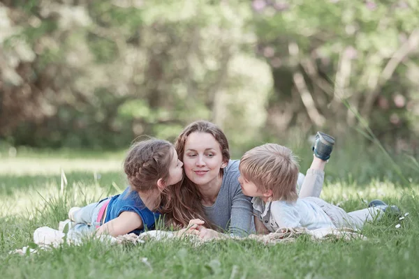 Madre feliz con sus bebés acostados en el césped en un día de verano —  Fotos de Stock