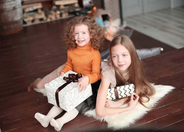 Dos hermanas pequeñas con cajas de regalo, sentadas en el suelo en una acogedora sala de estar. — Foto de Stock