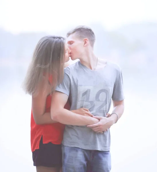 Joven pareja besándose mientras de pie en la orilla del lago de la ciudad — Foto de Stock