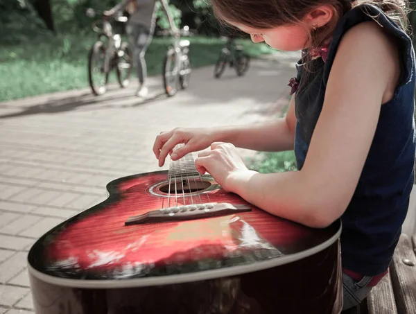 Kleines Mädchen mit Gitarre sitzt auf einer Parkbank — Stockfoto