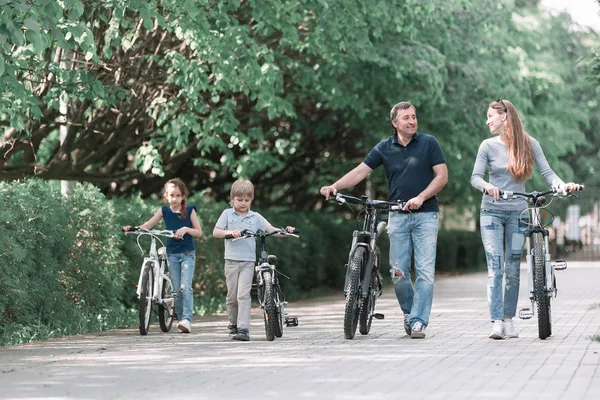 Familia moderna con sus bicicletas a pie por el parque de la ciudad — Foto de Stock