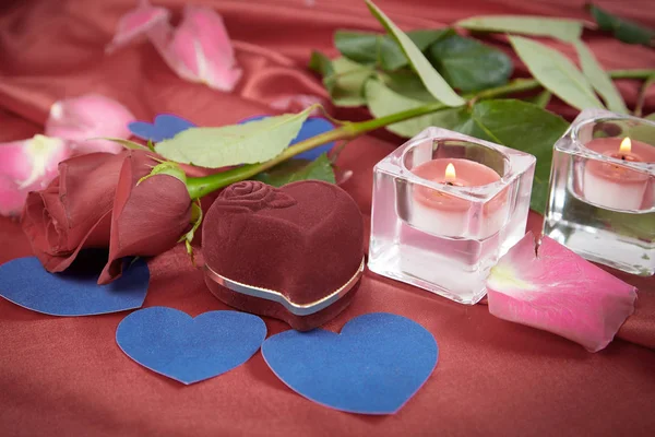 Dos velas y una rosa sobre un fondo de seda rojo —  Fotos de Stock