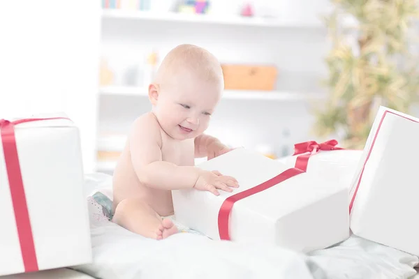 Pretty baby plays with gift boxes sitting on the couch — Stock Photo, Image