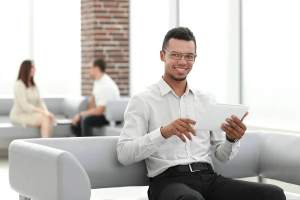 Uomo moderno utilizza un tablet digitale seduto nella hall dell'ufficio . — Foto Stock