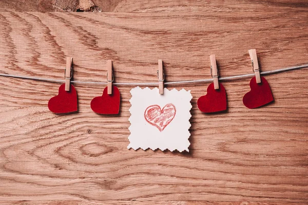 Folha em branco e corações em clothespins em fundo de madeira — Fotografia de Stock