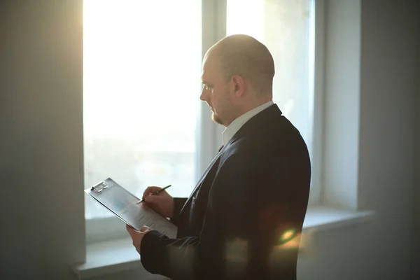 Adulto hombre de negocios firma documento de pie cerca de ventana de oficina . —  Fotos de Stock