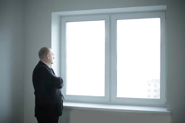 Pensativo hombre de negocios mirando una ventana de oficina en blanco —  Fotos de Stock