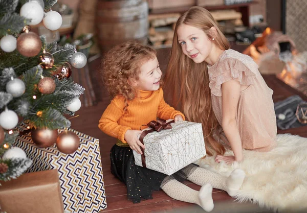 Twee mooie zussen met cadeautjes zitten op de vloer op kerstavond — Stockfoto