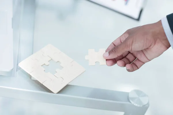 Close-up. de zakenman is een puzzel, zitten achter een bureau. — Stockfoto