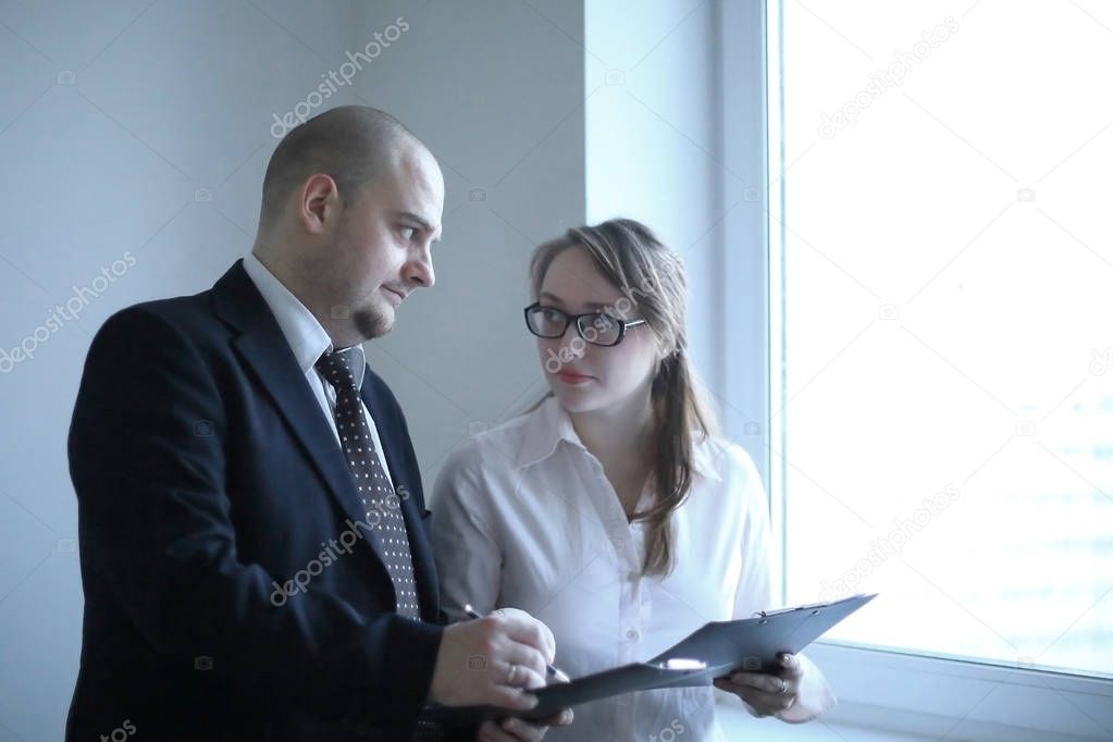 surprised businessman and assistant discussing business documents standing near office window
