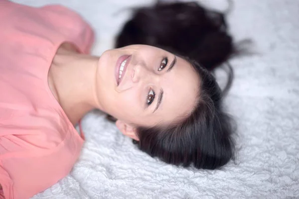 Close up .thoughtful young woman lying on white carpet in living room — стоковое фото