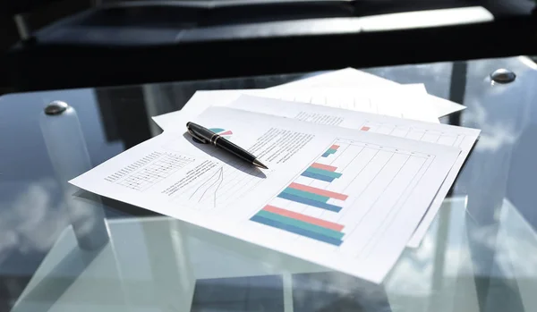 Gráfico financeiro e caneta na mesa de vidro no escritório — Fotografia de Stock