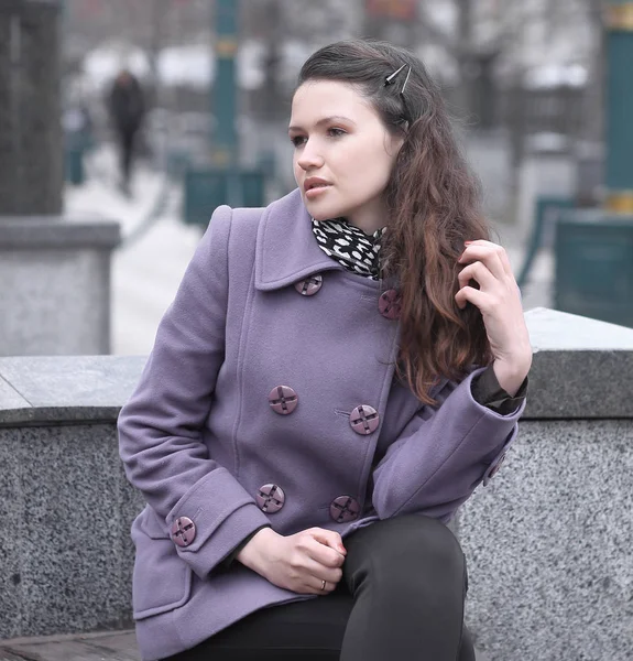 Женщина в модном пальто сидит на скамейке в городе — стоковое фото
