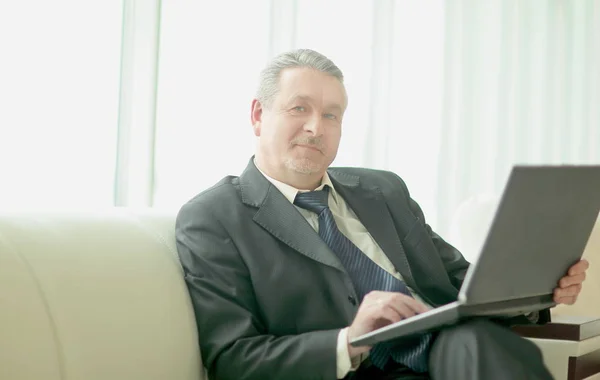 Succesvolle zakenman met laptop zitting in de lobby van het kantoor — Stockfoto