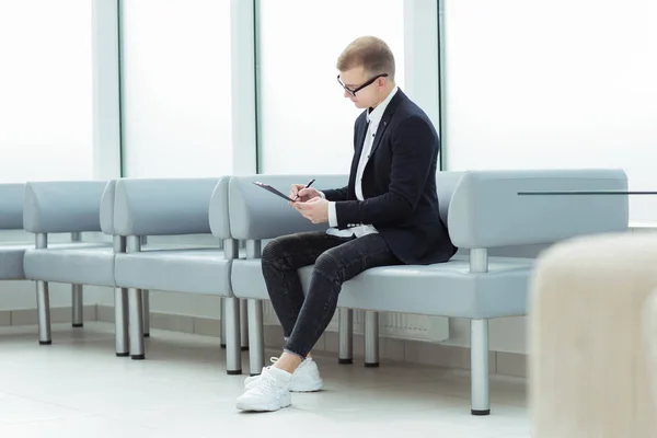 Hombre de negocios leyendo un documento de negocios sentado en el vestíbulo de la oficina —  Fotos de Stock