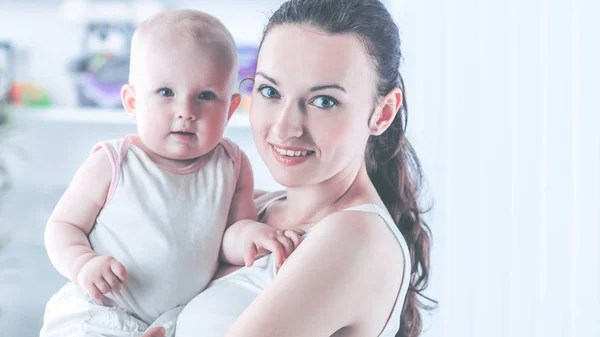 Retrato de uma mãe feliz com um bebê de anos em seus braços no fundo de uma sala de crianças — Fotografia de Stock