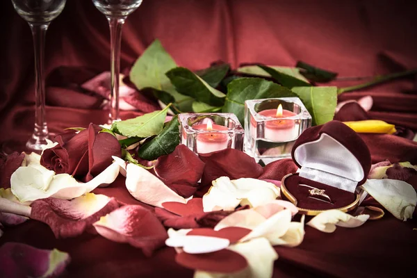 candles, red rose and ring on rose petals background.
