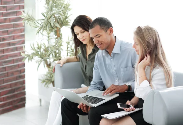 Grupo de negocios mirando a la computadora portátil mientras está sentado en el vestíbulo del hotel — Foto de Stock