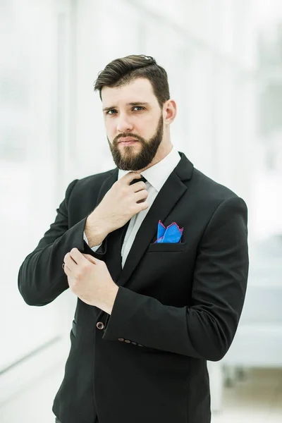 Erfolgreicher Geschäftsmann justiert seine Krawatte, während er im hellen Büro am Fenster steht. — Stockfoto