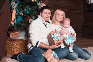 mutlu aile ile Noel arifesinde Noel ağacının yanında oturan hediye kutuları