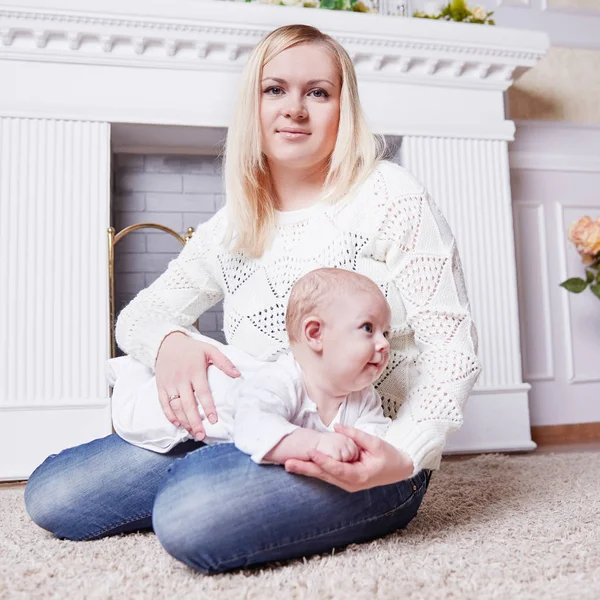 Madre con bebé sentado cerca de la chimenea en una acogedora sala de estar — Foto de Stock