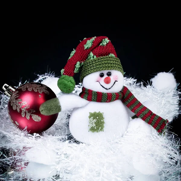 Leuke speelgoed sneeuwpop en kerst bal op een zwarte achtergrond. — Stockfoto