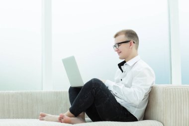 gülümseyen adam üstünde a laptop oturma odasında çalışıyor.