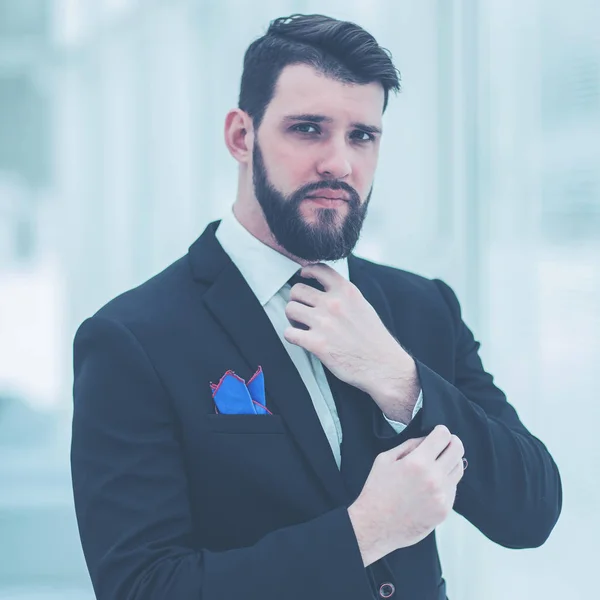 Erfolgreicher Geschäftsmann justiert seine Krawatte, während er im hellen Büro am Fenster steht. — Stockfoto