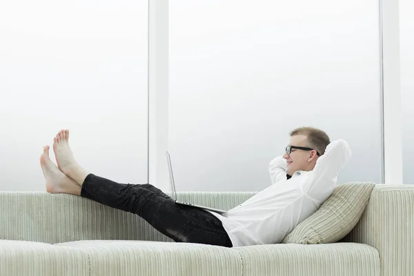现代男子与笔记本电脑躺在沙发上的客厅 — 图库照片