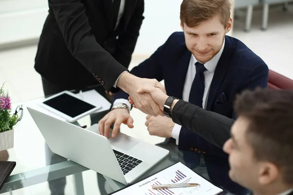 Финансовые партнеры пожимают друг другу руки за столом в офисе — стоковое фото