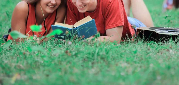 S úsměvem pár studentů čtení knihy ležící na trávě — Stock fotografie